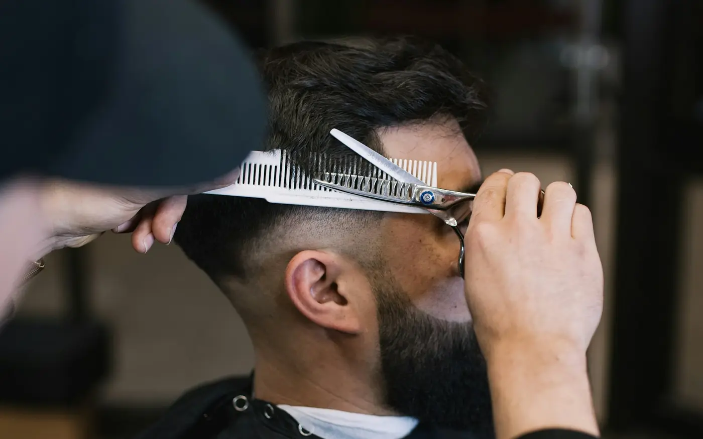 Barber lifting hair with a comb and trimming with scissors over a fresh fade
